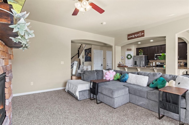 carpeted living room featuring a stone fireplace and ceiling fan