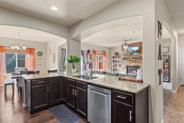 kitchen with dark hardwood / wood-style flooring, stainless steel dishwasher, a brick fireplace, sink, and decorative light fixtures