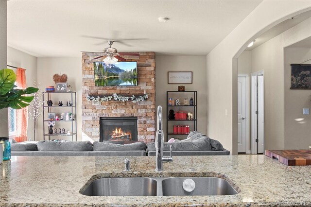 kitchen featuring light stone counters, sink, a fireplace, and ceiling fan