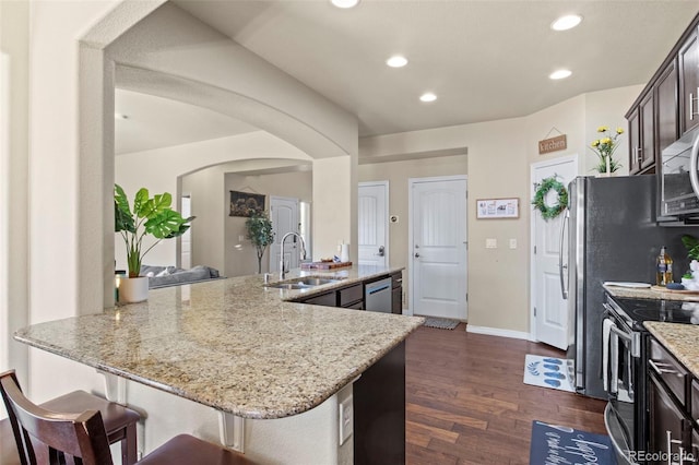 kitchen with dark wood-type flooring, sink, light stone countertops, dark brown cabinetry, and appliances with stainless steel finishes