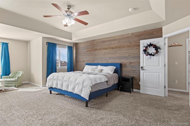 bedroom featuring wooden walls, a raised ceiling, carpet floors, and ceiling fan