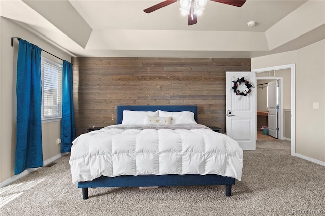 carpeted bedroom featuring ceiling fan, a tray ceiling, and wood walls