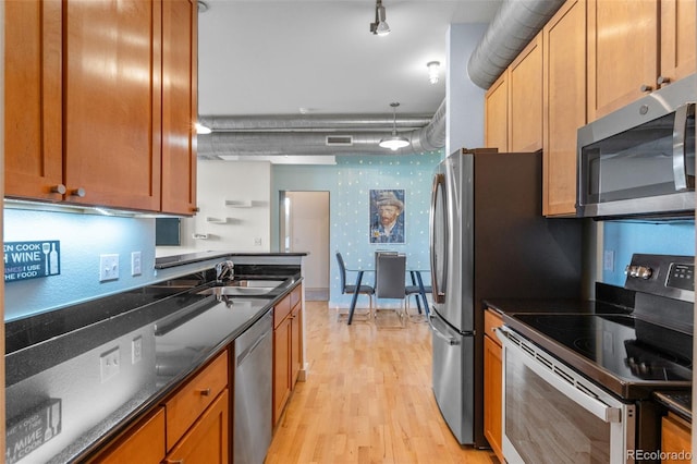 7700 E 29th Ave Unit 304, Denver, CO 80238 - kitchen featuring appliances with stainless steel finishes, light wood-style floors, dark stone counters, and brown cabinetry