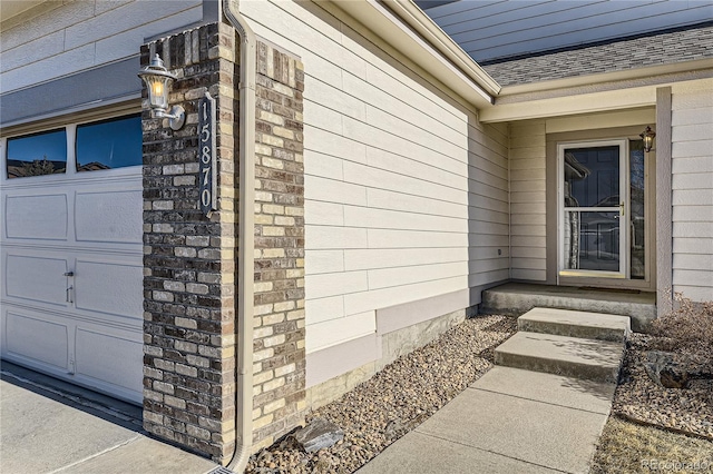 property entrance featuring an attached garage, brick siding, and roof with shingles