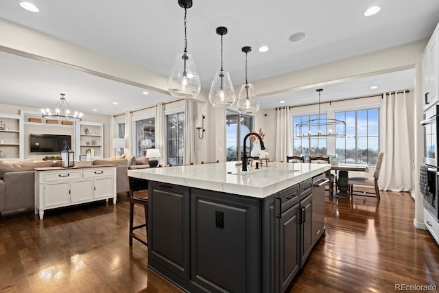 kitchen with a center island with sink, a chandelier, sink, pendant lighting, and light stone countertops