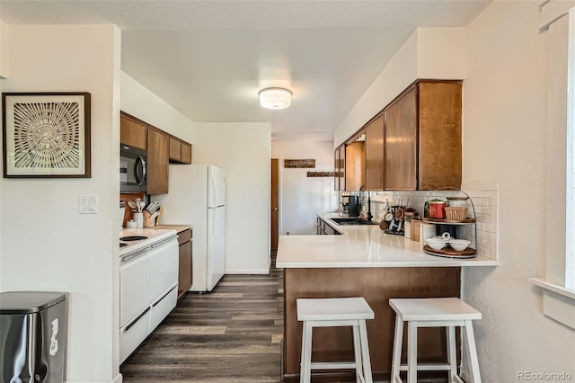 28669 Mountain View Rd, Conifer, CO 80433 - kitchen featuring white appliances, light countertops, a breakfast bar, dark wood finished floors, and brown cabinetry