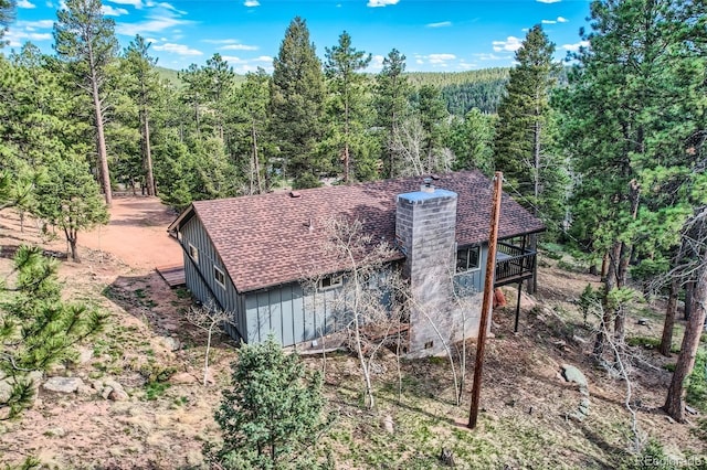 28669 Mountain View Rd, Conifer, CO 80433 - rear view of house featuring board and batten siding, a wooded view, a chimney, and a shingled roof