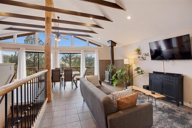 living room featuring ceiling fan, vaulted ceiling with beams, light tile patterned floors, and a wood stove