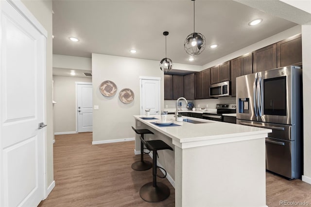 kitchen with a sink, light wood-style floors, dark brown cabinetry, appliances with stainless steel finishes, and light countertops