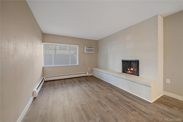 unfurnished living room featuring a brick fireplace, hardwood / wood-style flooring, a wall mounted AC, and a baseboard heating unit