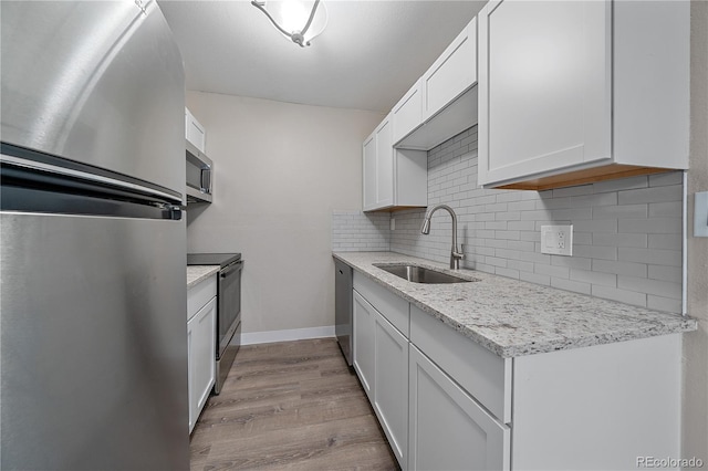 kitchen with appliances with stainless steel finishes, light stone counters, sink, white cabinets, and light hardwood / wood-style floors