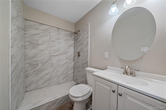 bathroom featuring a tile shower, vanity, and toilet