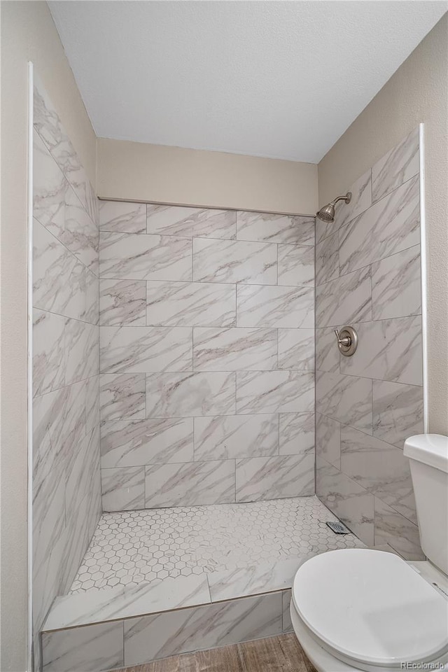 bathroom with a tile shower and toilet