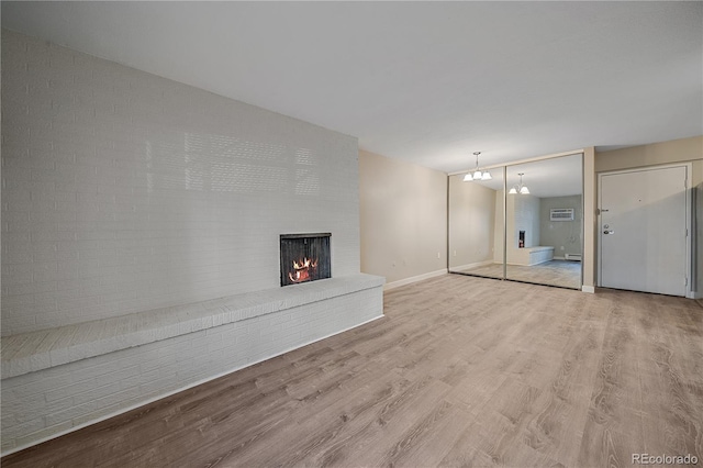 unfurnished living room featuring baseboards, a notable chandelier, wood finished floors, and a fireplace