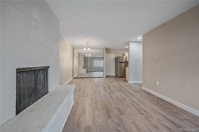 unfurnished living room with light wood-style floors, a brick fireplace, and baseboards