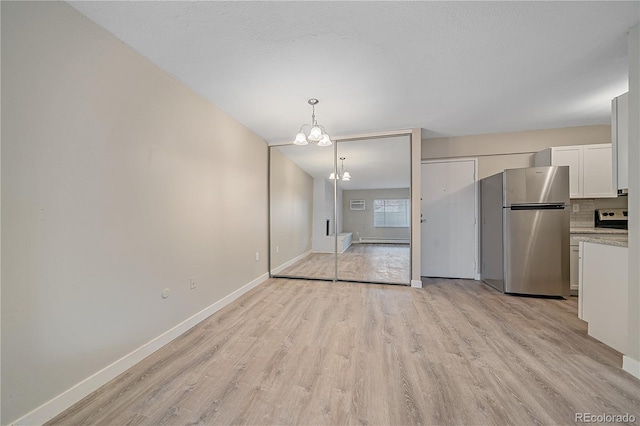 unfurnished dining area with a chandelier, light wood-type flooring, a baseboard radiator, and baseboards
