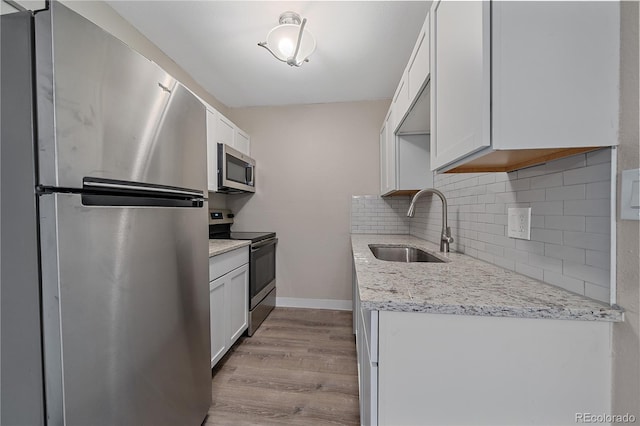 kitchen featuring tasteful backsplash, wood finished floors, a sink, appliances with stainless steel finishes, and white cabinetry