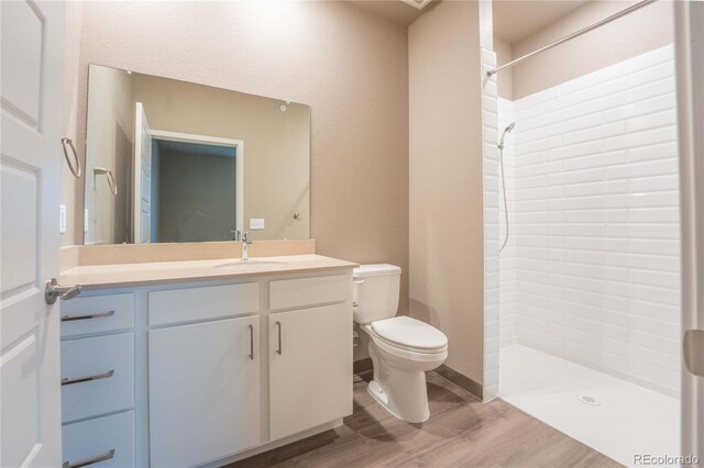 bathroom featuring vanity, wood-type flooring, toilet, and tiled shower