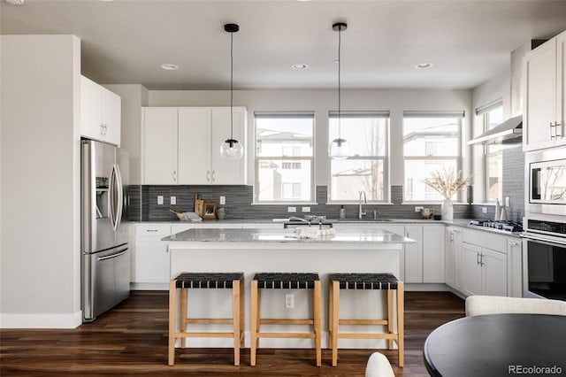 kitchen with a kitchen breakfast bar, appliances with stainless steel finishes, white cabinetry, light stone counters, and a kitchen island