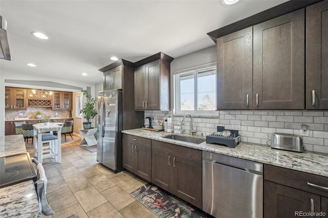 kitchen featuring sink, appliances with stainless steel finishes, dark brown cabinetry, light stone counters, and decorative backsplash