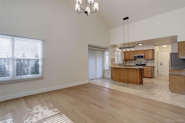 6055 W Warren, Lakewood, CO 80227 - kitchen featuring appliances with stainless steel finishes, high vaulted ceiling, brown cabinetry, a chandelier, and a peninsula
