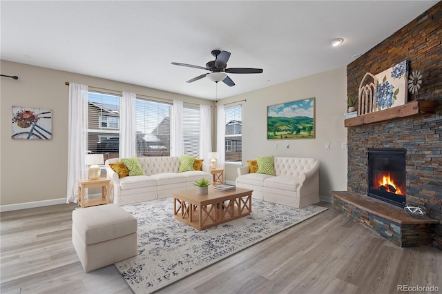 living area featuring a stone fireplace, ceiling fan, light wood-style flooring, and baseboards