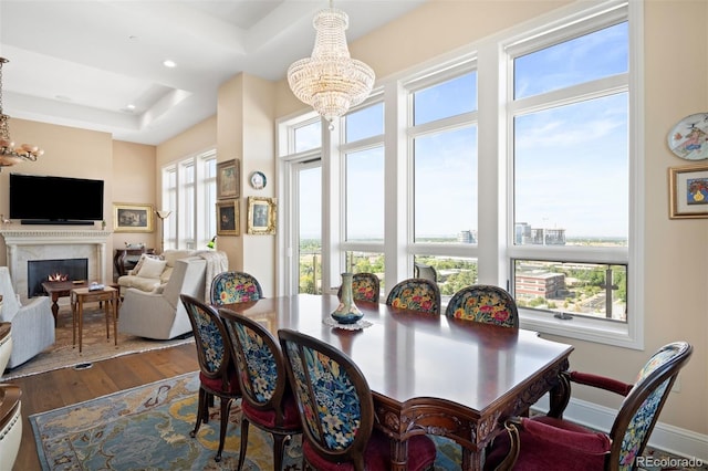 dining area featuring a raised ceiling, wood finished floors, a high end fireplace, and a notable chandelier