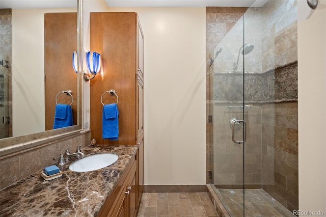 full bathroom featuring a stall shower, backsplash, vanity, and baseboards