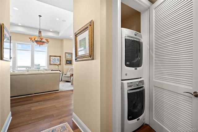 laundry area featuring laundry area, baseboards, dark wood-type flooring, stacked washing maching and dryer, and recessed lighting