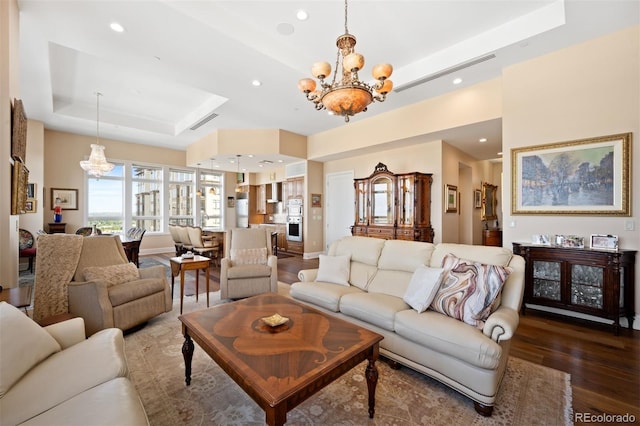 living area featuring visible vents, dark wood finished floors, a tray ceiling, a notable chandelier, and recessed lighting