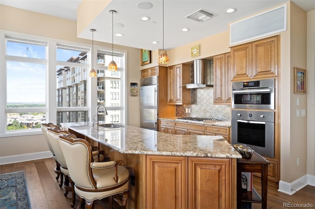 kitchen with stainless steel appliances, visible vents, brown cabinetry, a sink, and wall chimney range hood