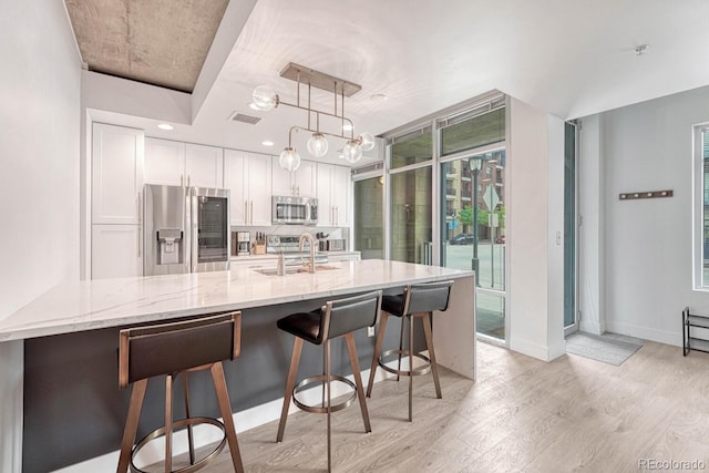 1700 Bassett St Unit 101, Denver, CO 80202 - kitchen with appliances with stainless steel finishes, a sink, light wood-type flooring, white cabinets, and a breakfast bar