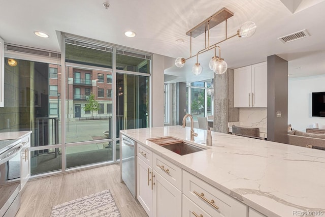 1700 Bassett St Unit 101, Denver, CO 80202 - kitchen featuring a sink, stainless steel appliances, a wall of windows, light stone countertops, and white cabinetry