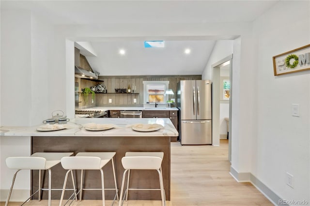 kitchen with light hardwood / wood-style floors, kitchen peninsula, appliances with stainless steel finishes, a breakfast bar area, and vaulted ceiling