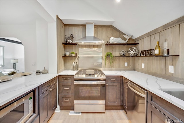 kitchen featuring wall chimney exhaust hood, lofted ceiling, stainless steel appliances, and light stone counters