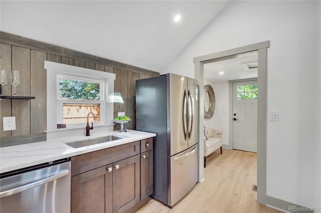 kitchen featuring vaulted ceiling, light stone countertops, stainless steel appliances, light hardwood / wood-style flooring, and sink