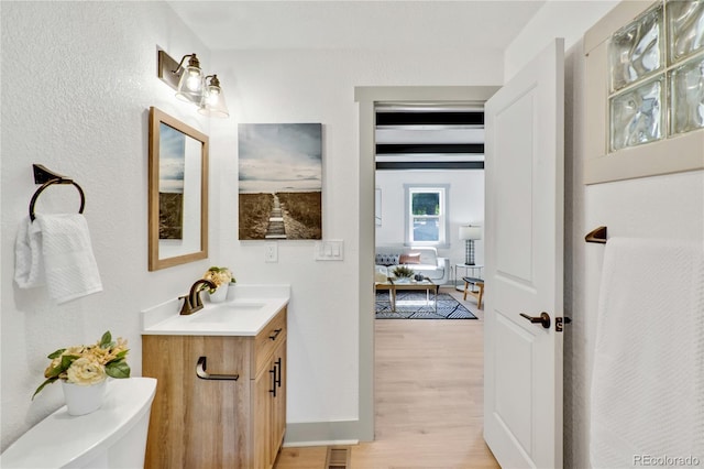 bathroom featuring beamed ceiling, vanity, hardwood / wood-style floors, and toilet