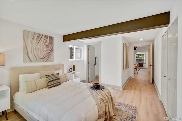 bedroom featuring light wood-type flooring, beam ceiling, and a closet