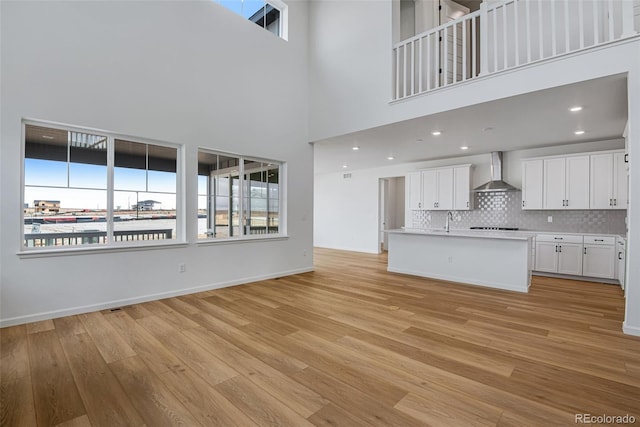 unfurnished living room featuring sink, light hardwood / wood-style flooring, and a towering ceiling