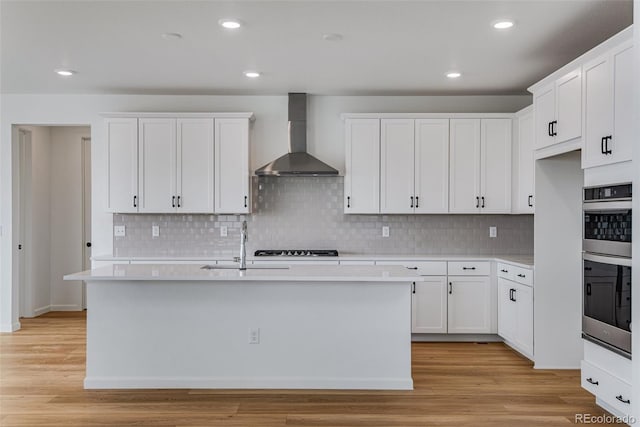 kitchen with white cabinetry, light hardwood / wood-style floors, and wall chimney exhaust hood