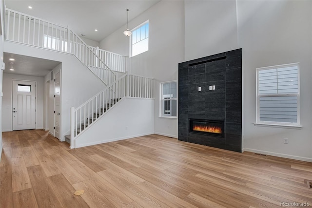 unfurnished living room featuring a towering ceiling, light hardwood / wood-style flooring, and a tile fireplace