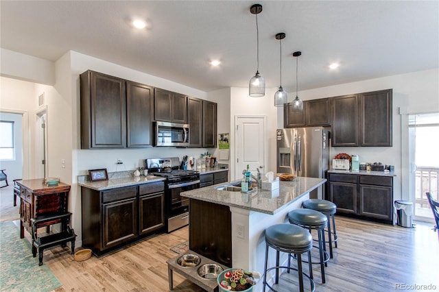 kitchen featuring light wood-type flooring, stainless steel appliances, a kitchen island with sink, sink, and decorative light fixtures