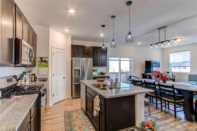 kitchen featuring pendant lighting, a center island with sink, light hardwood / wood-style flooring, appliances with stainless steel finishes, and dark brown cabinetry