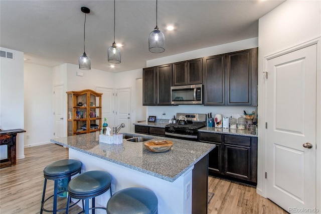 kitchen featuring a kitchen island with sink, sink, stone countertops, and appliances with stainless steel finishes