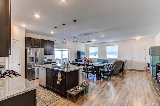 kitchen featuring sink, stainless steel appliances, light stone counters, a center island with sink, and dark brown cabinets