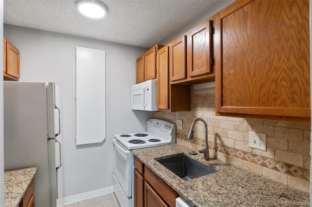 kitchen featuring a textured ceiling, tasteful backsplash, sink, white appliances, and light stone countertops