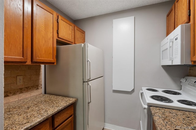 kitchen with a textured ceiling, backsplash, white appliances, and light stone countertops