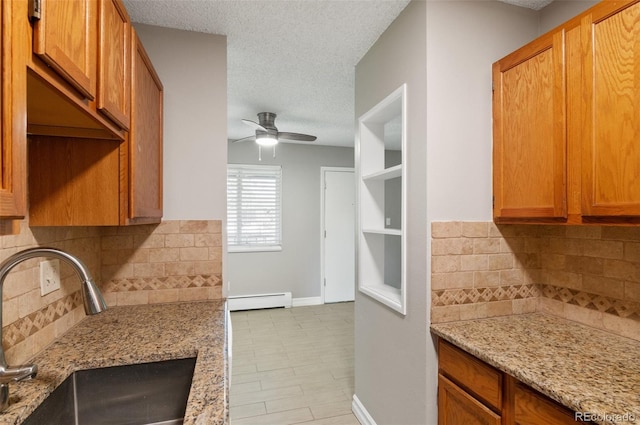 kitchen featuring a baseboard heating unit, light stone counters, sink, decorative backsplash, and ceiling fan