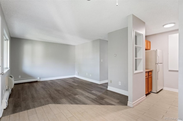 empty room featuring a textured ceiling, light hardwood / wood-style floors, and a baseboard heating unit