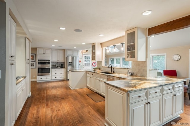 7750 S Glencoe Way, Centennial, CO 80122 - kitchen featuring appliances with stainless steel finishes, a peninsula, wood finished floors, glass insert cabinets, and tasteful backsplash
